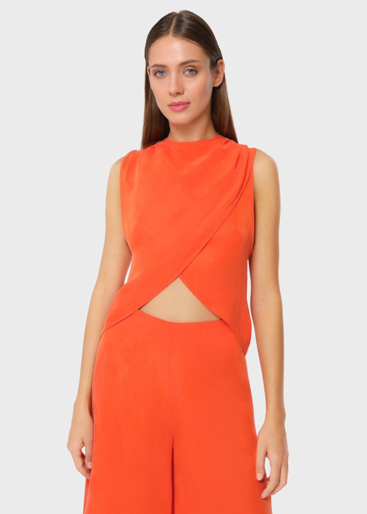Bright orange sleeveless wrap top with a high neckline and subtle draping. Overlap front detail creates a soft cutout at the waist, paired with matching wide-leg pants for a bold, modern set.