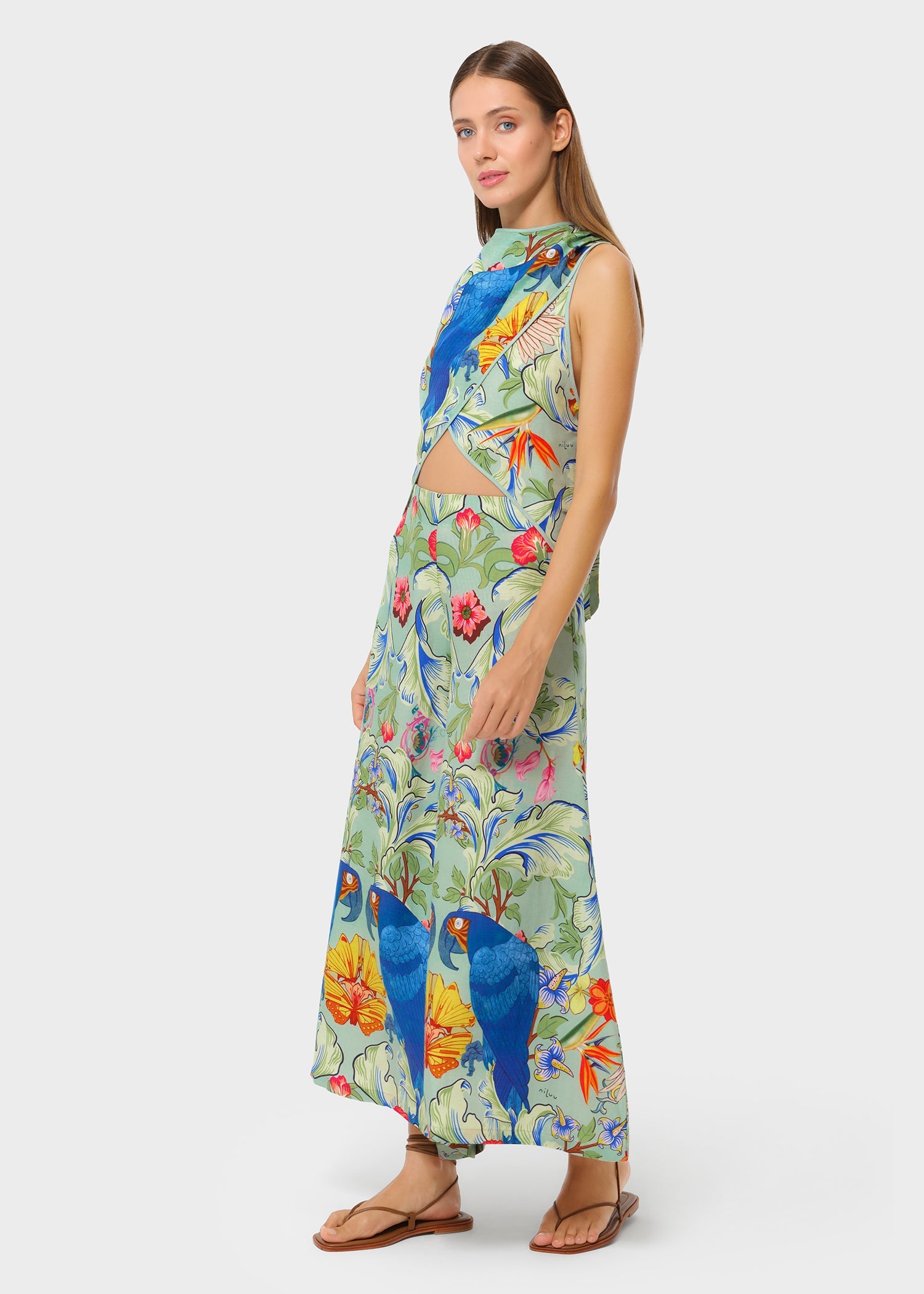 Side view of the printed co-ord set featuring bold florals and blue parrots. Sleeveless crossover top with a waist cutout, paired with flowing wide-leg pants.
