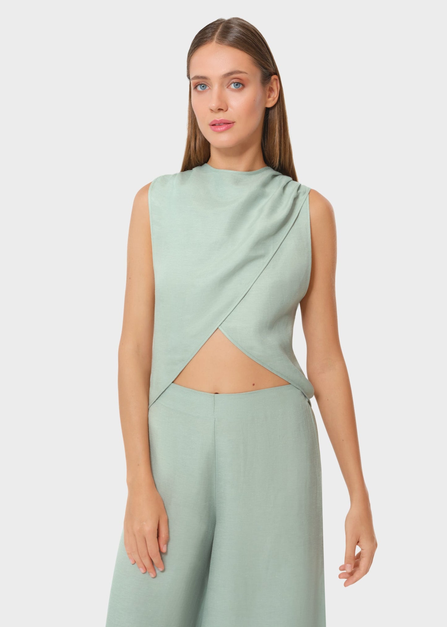 Woman wearing a mint green sleeveless wrap crop top with a high neckline and matching wide-leg pants, resort-style set against a neutral background.