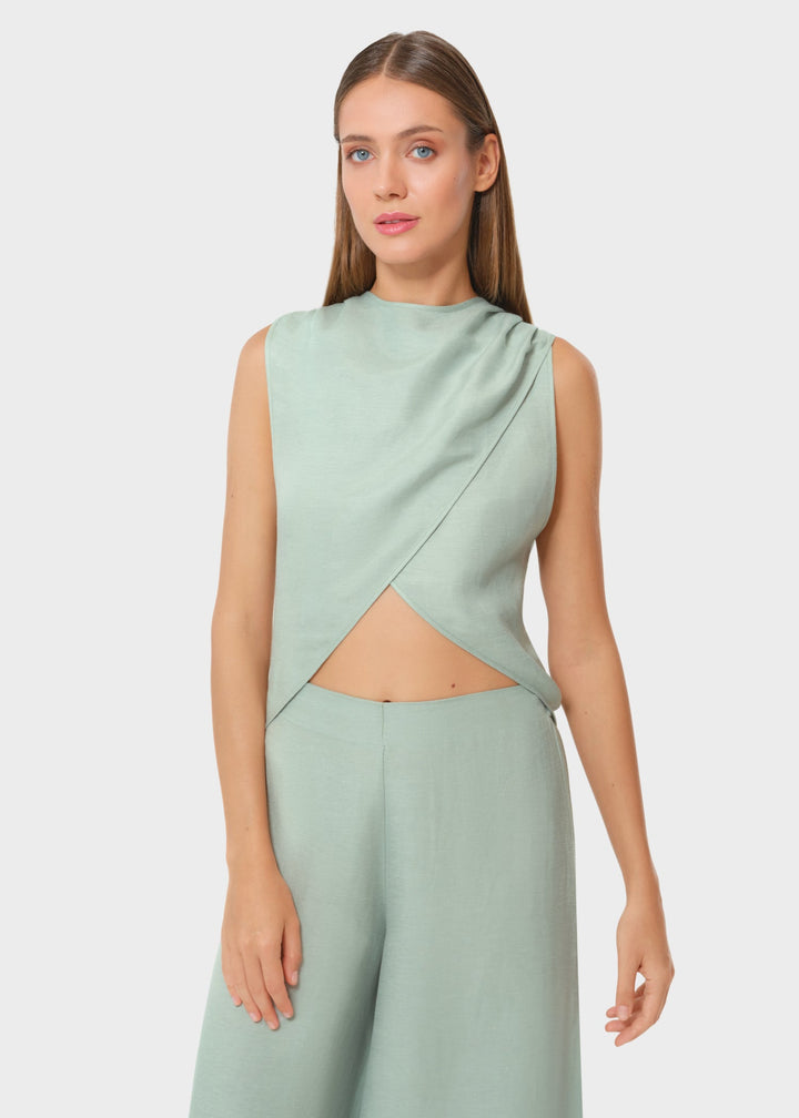 Woman wearing a mint green sleeveless wrap crop top with a high neckline and matching wide-leg pants, resort-style set against a neutral background.