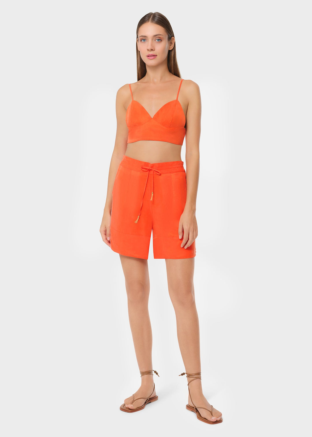 Model in bright orange bralette with matching lounge shorts, studio background