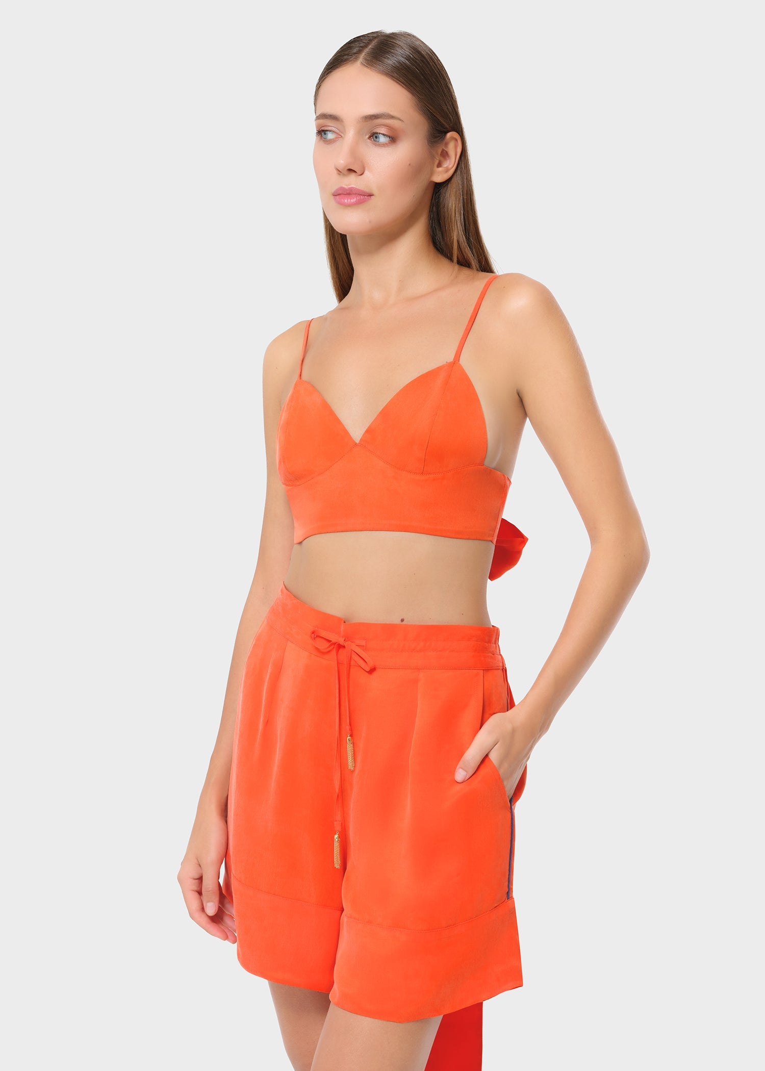 Model in bright orange bralette with matching lounge shorts, side view, studio background