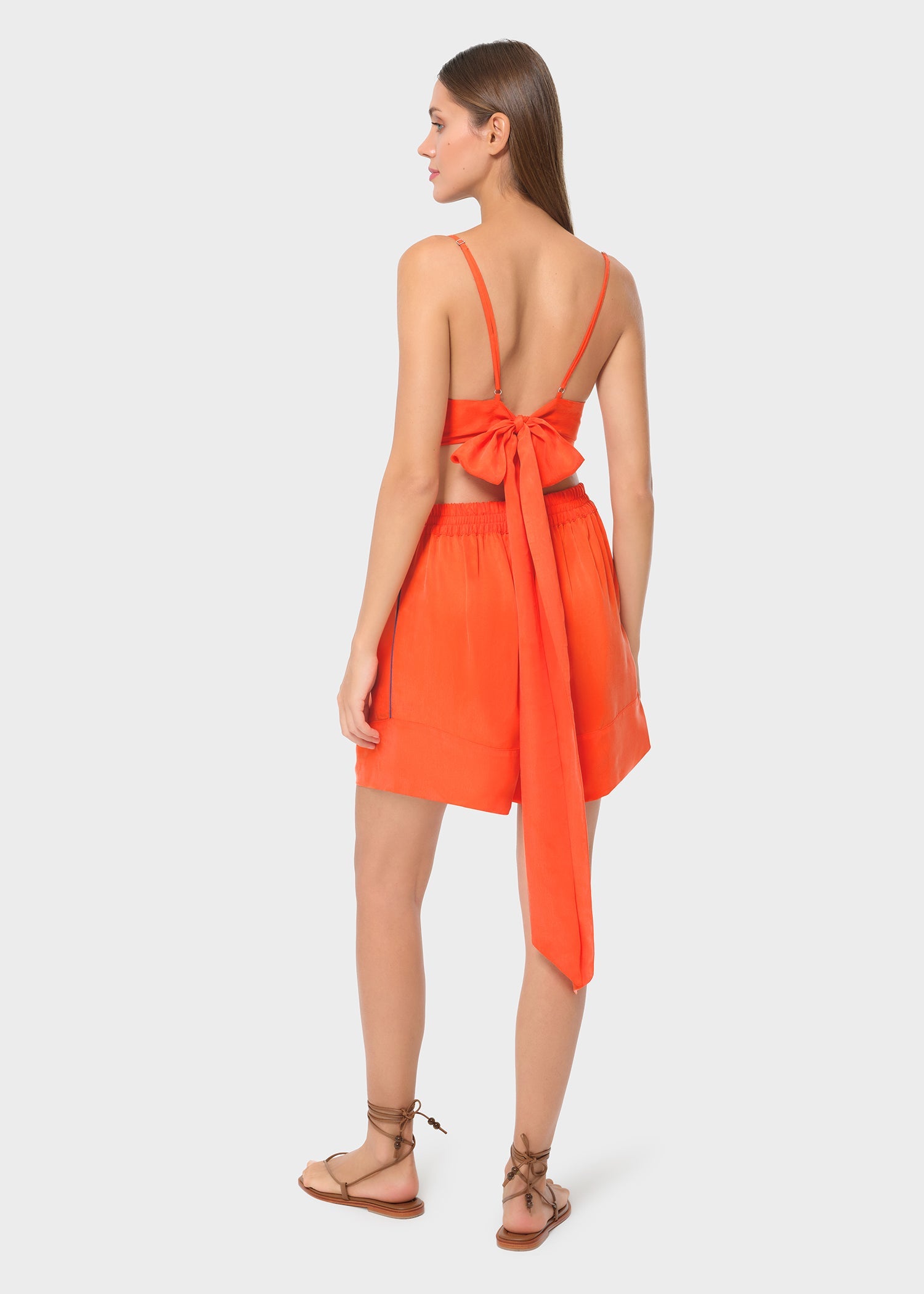 Back view of model in bright orange bralette with matching lounge shorts, studio background