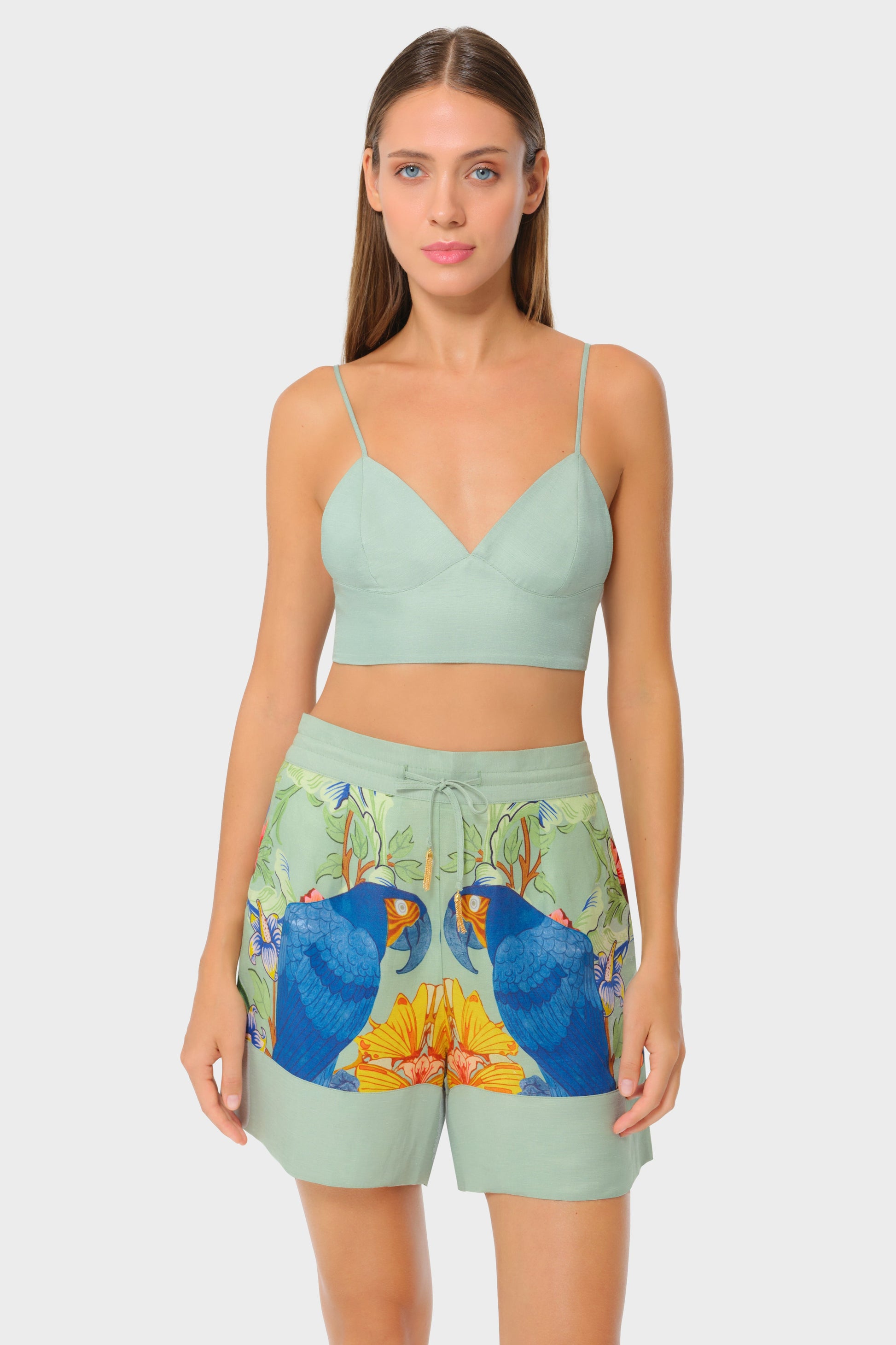 Model wearing a mint green bralette and printed short lounge shorts with blue parrot and floral design on a light background, front view.