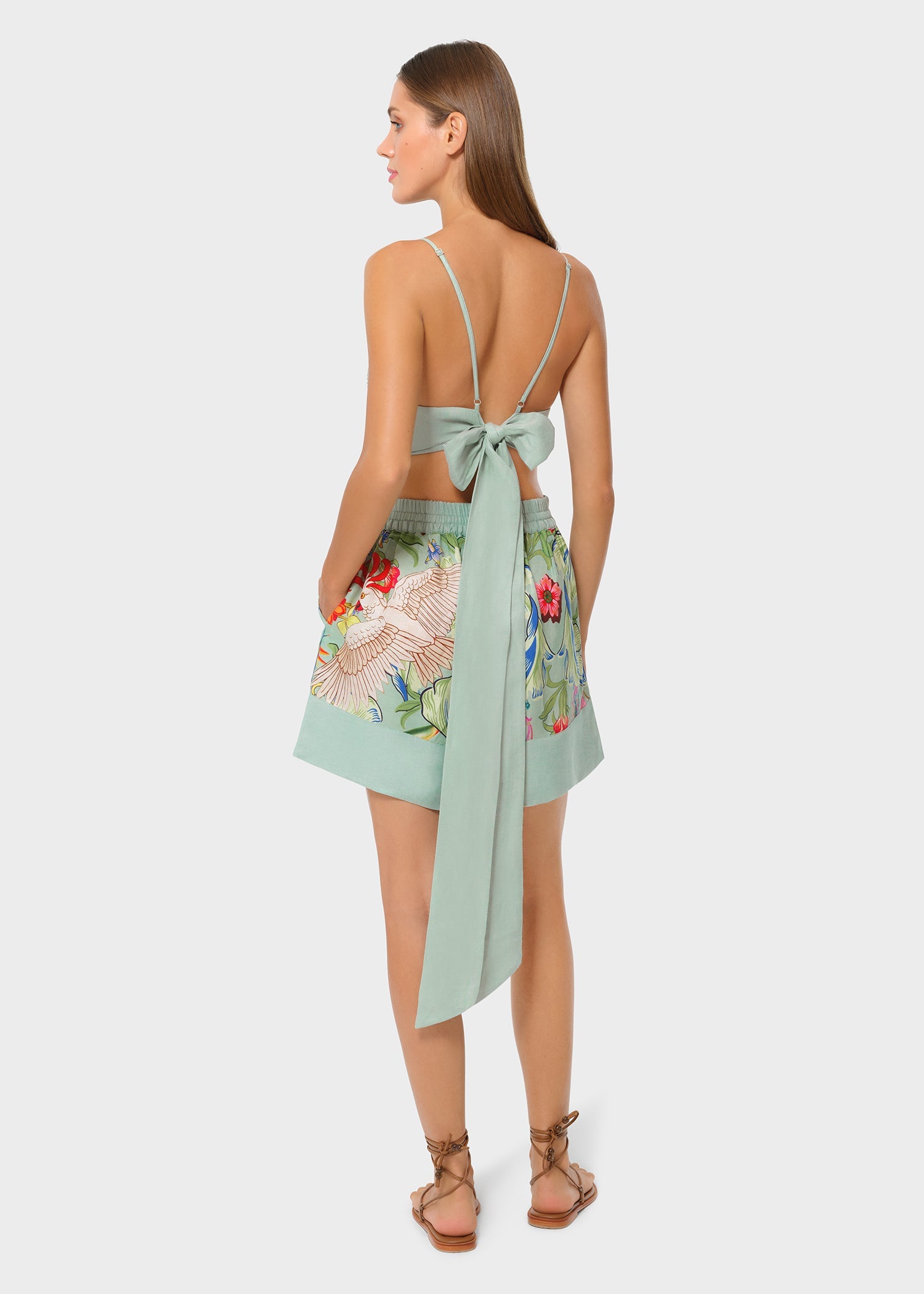Back view of mint green bralette with tie bow detail paired with tropical print high-waisted shorts.