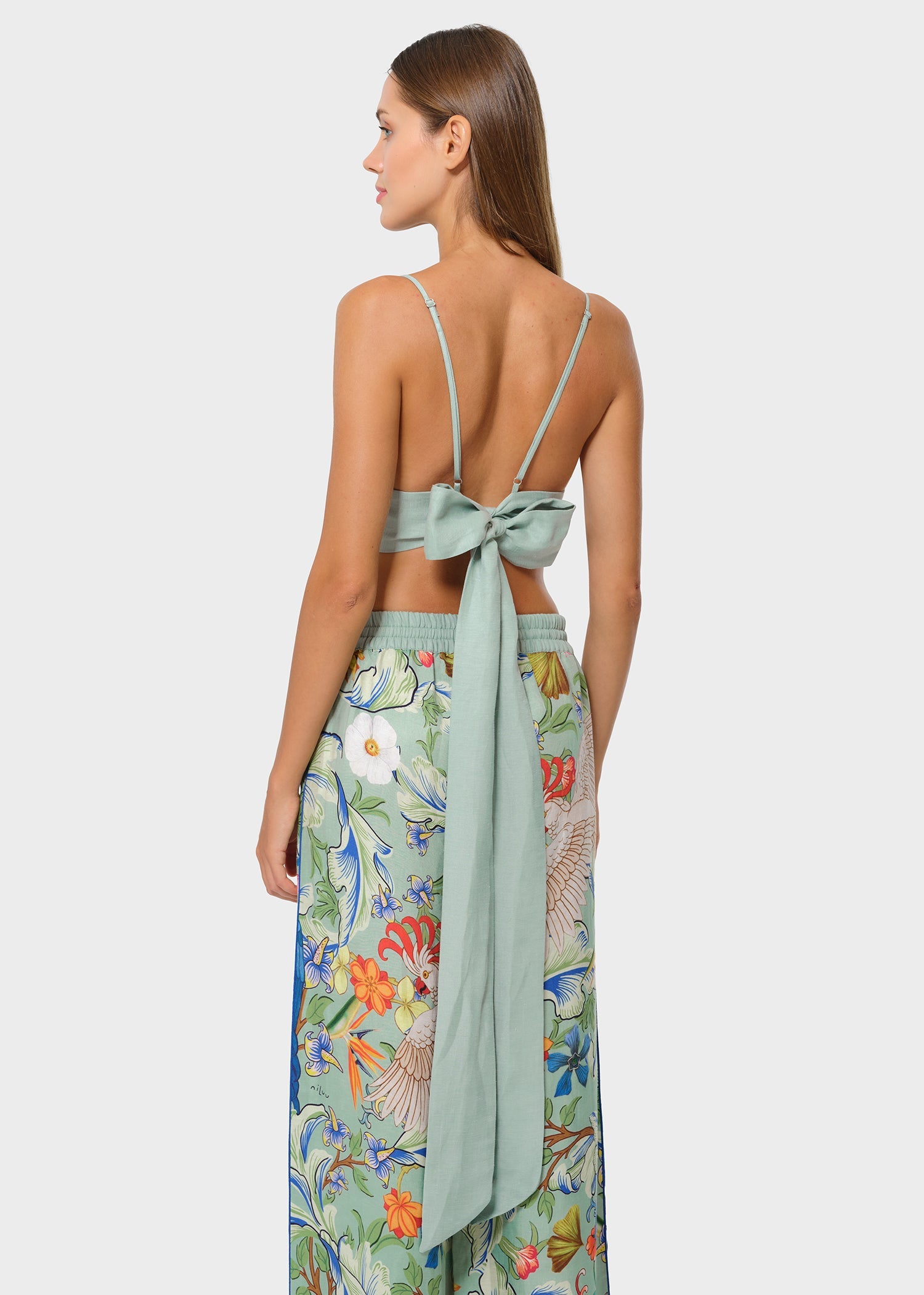 Woman wearing mint green vegan silk bralette with bow tie back and floral wide leg pants