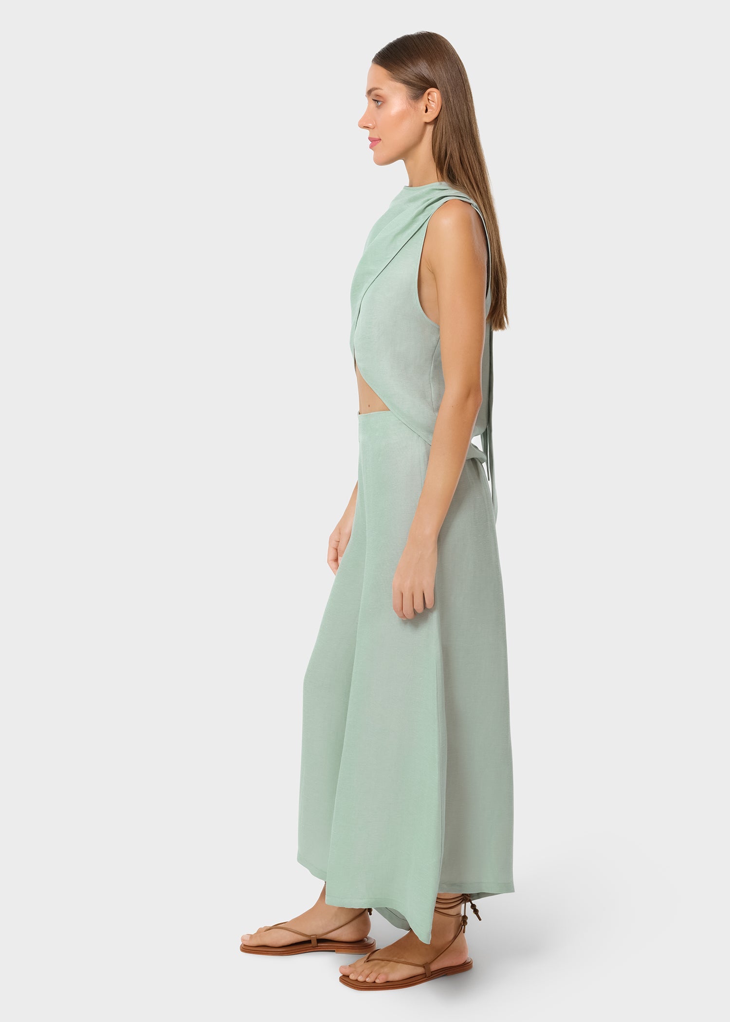 Side view of a woman in a mint sleeveless wrap top with a side cutout and matching wide-leg pants, styled with flat sandals in a studio setting.