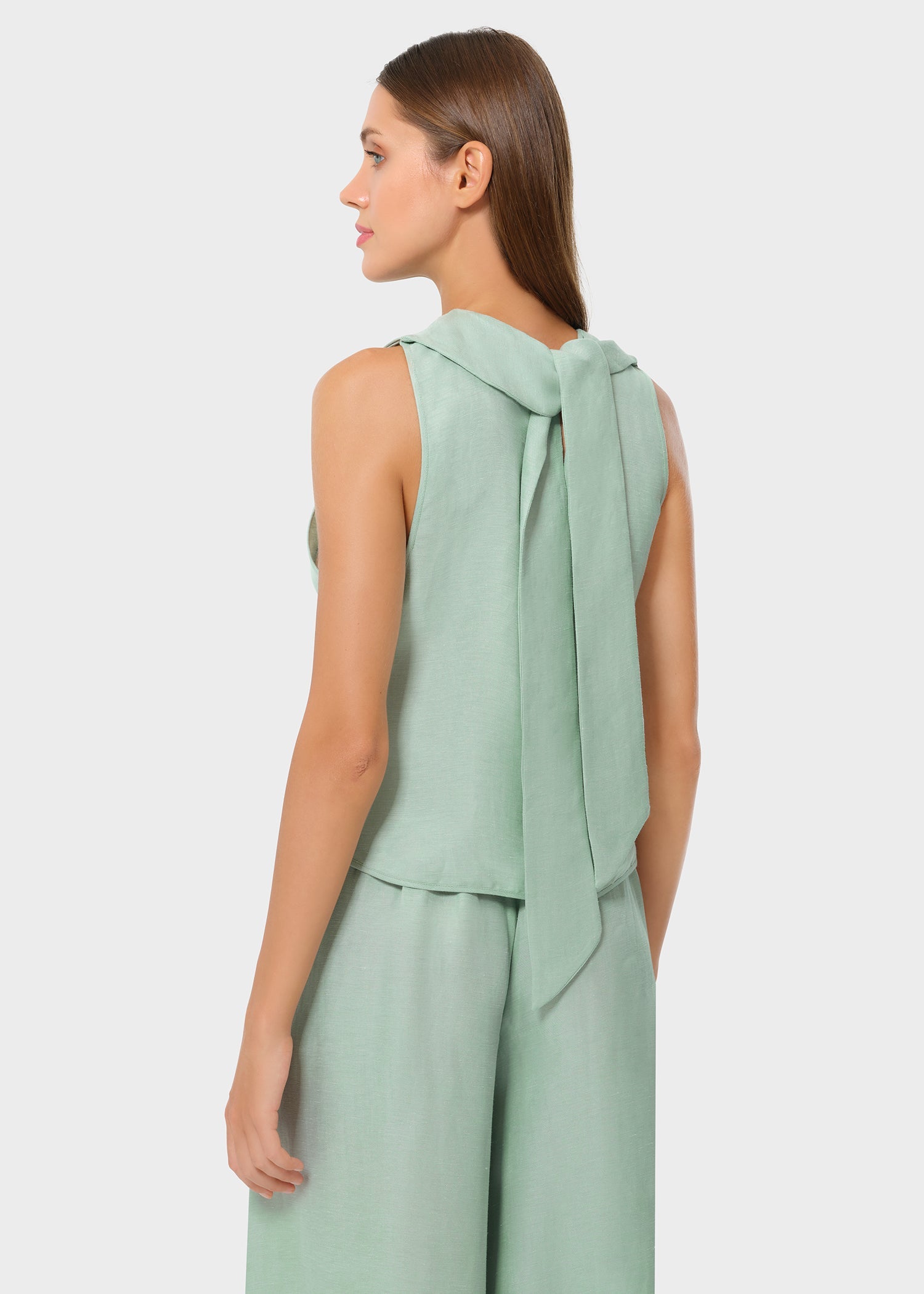 Back and side view of a woman wearing a mint sleeveless top with a long tie detail draping down the back, paired with matching wide-leg pants, shown in a studio setting.