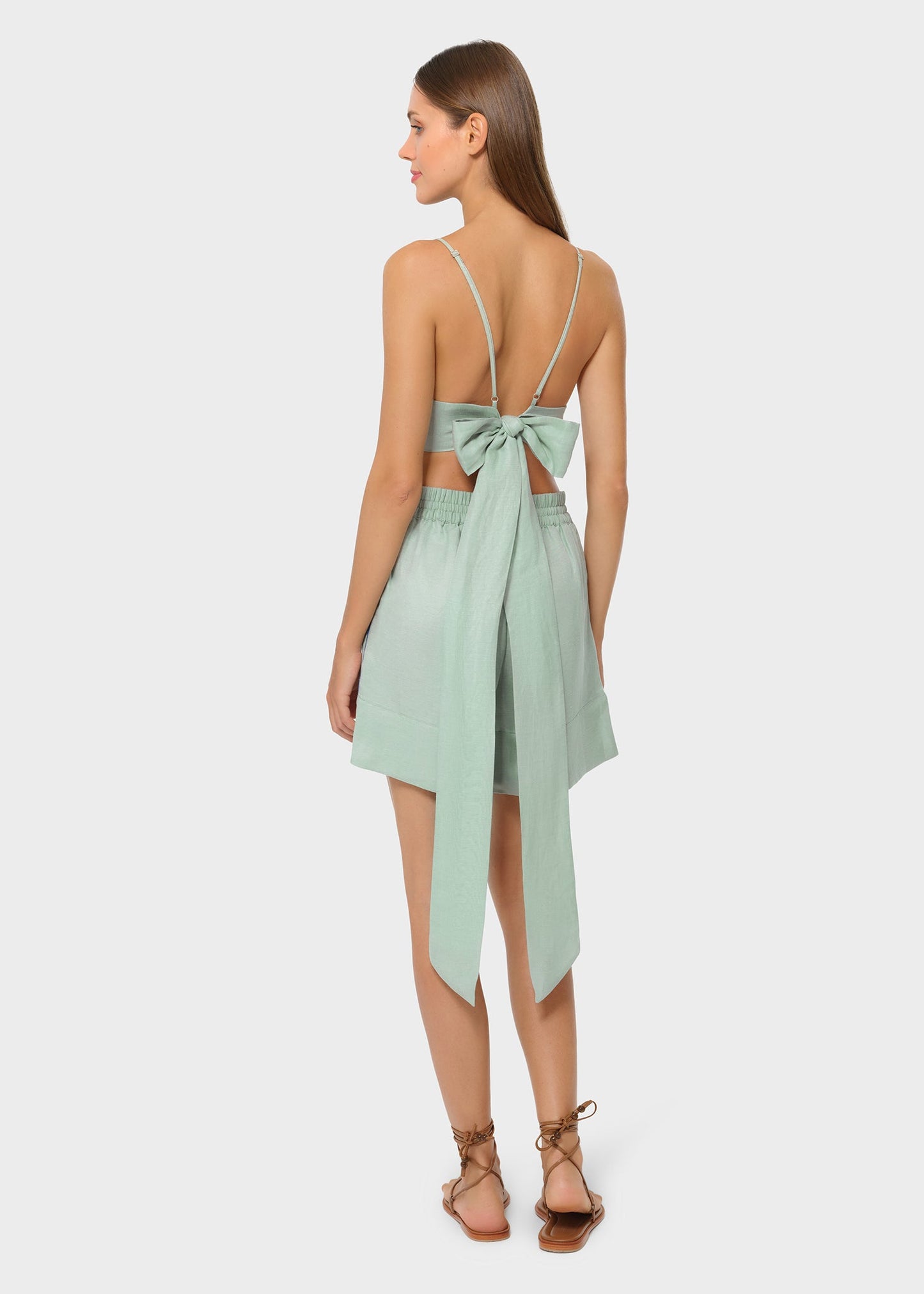 Back view of model in sage green bralette with bow tie and matching lounge shorts on studio background