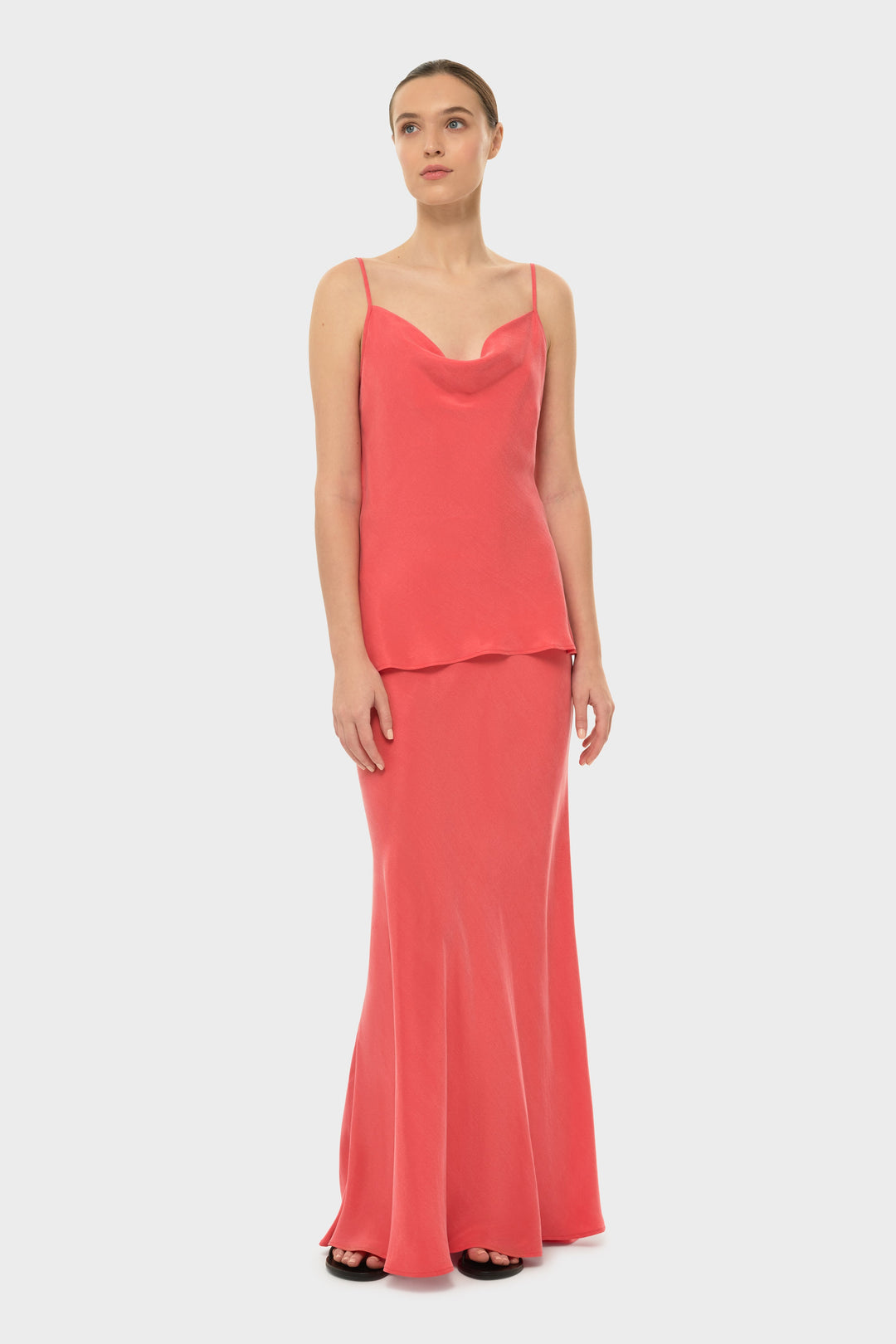 The model is wearing a black bikini top with a coral-colored maxi skirt.