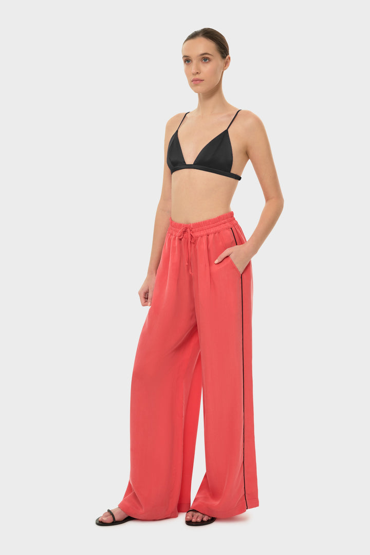 The model wears a black bikini top with coral drawstring pants featuring a black side stripe.