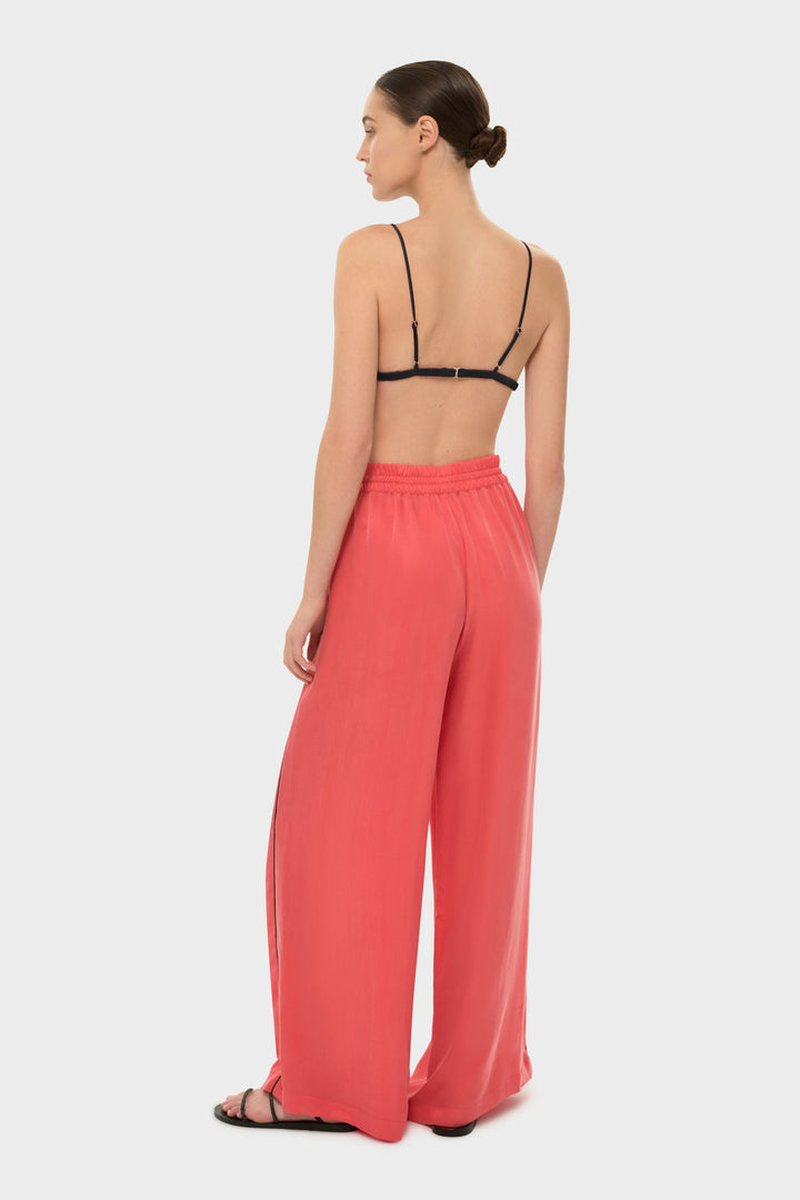 The model wears a black bikini top with coral drawstring pants featuring a black side stripe.