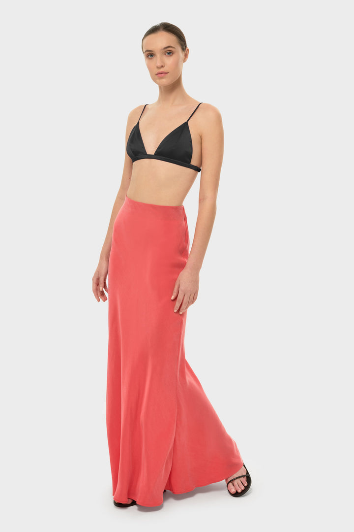 The model is wearing a black bikini top with a coral-colored maxi skirt.