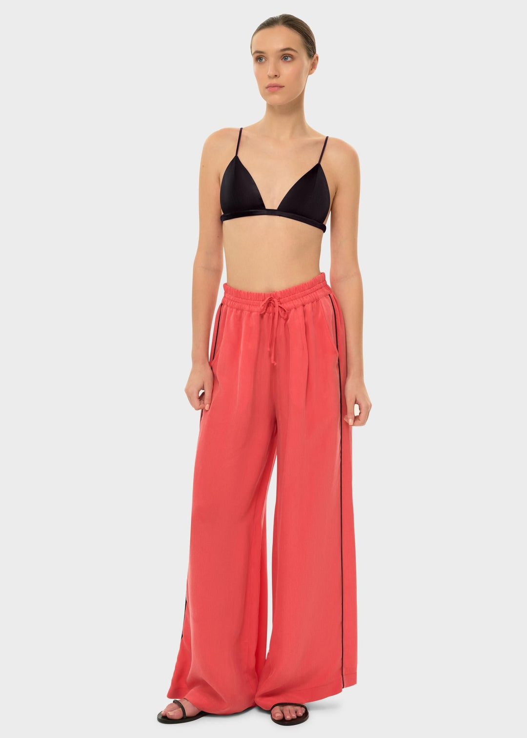 The model wears a black bikini top with coral drawstring pants featuring a black side stripe.