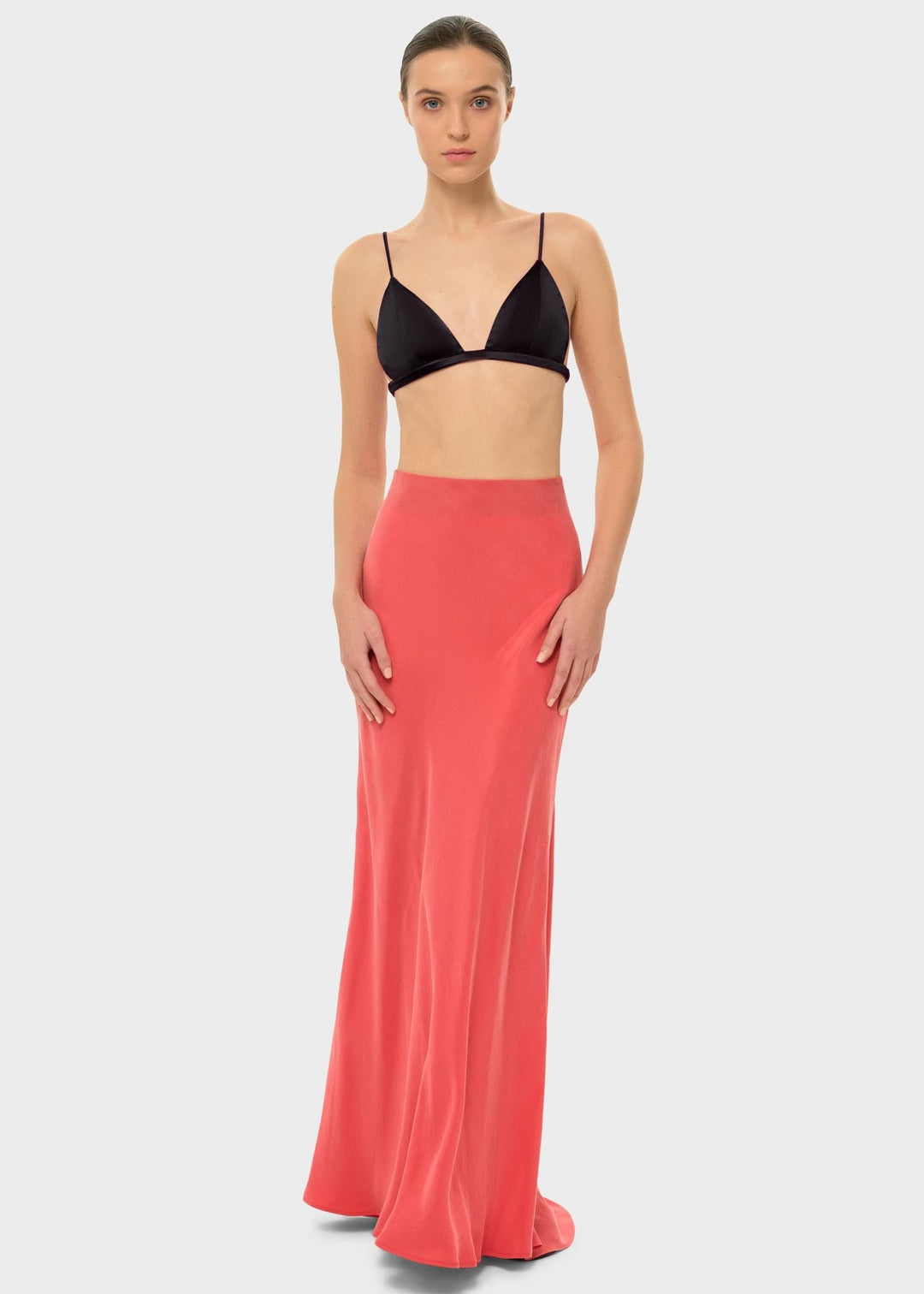 The model is wearing a black bikini top with a coral-colored maxi skirt.
