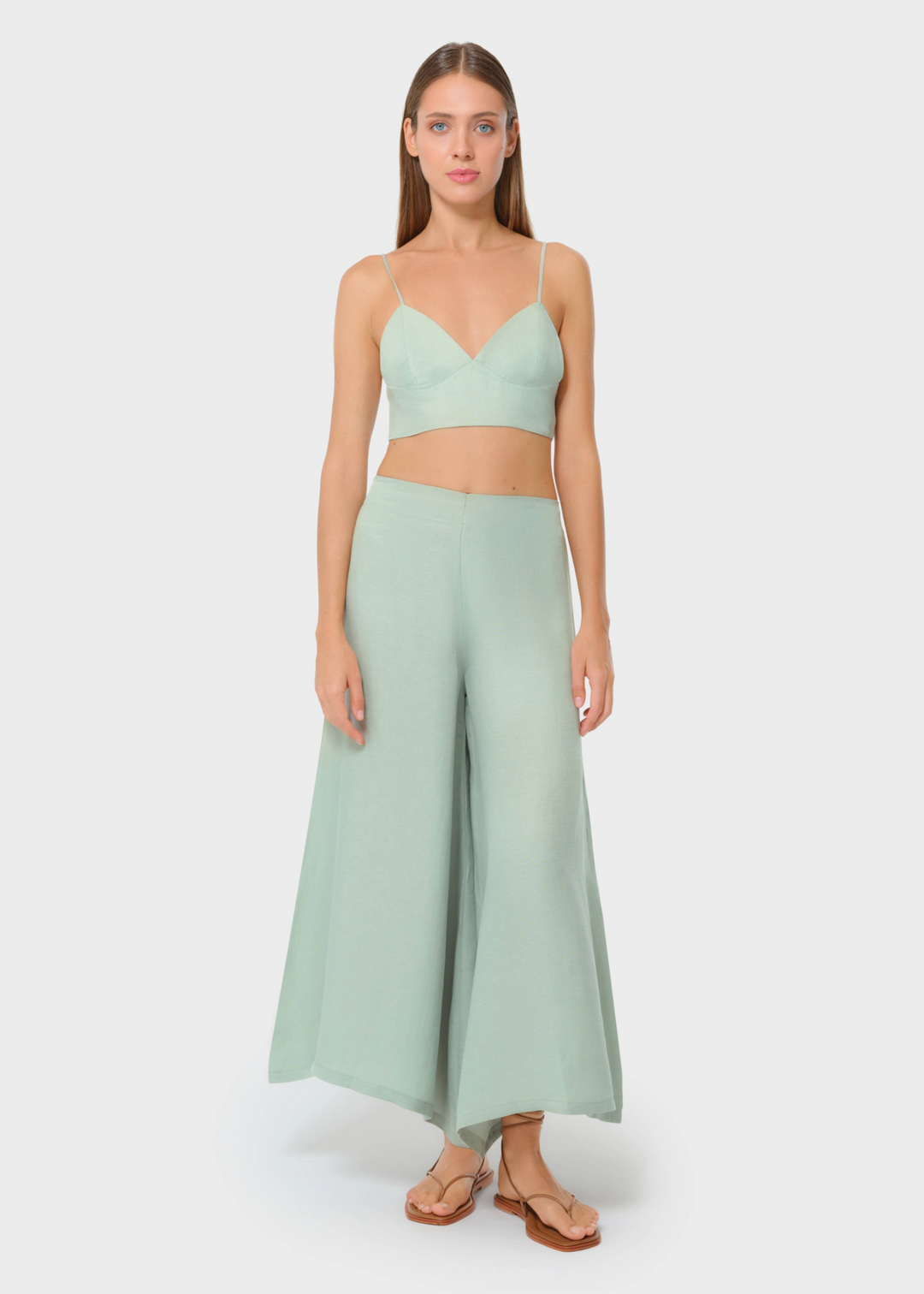 Model wearing a sage green bralette with matching high-waisted wide-leg pants, styled with flat sandals, studio background.