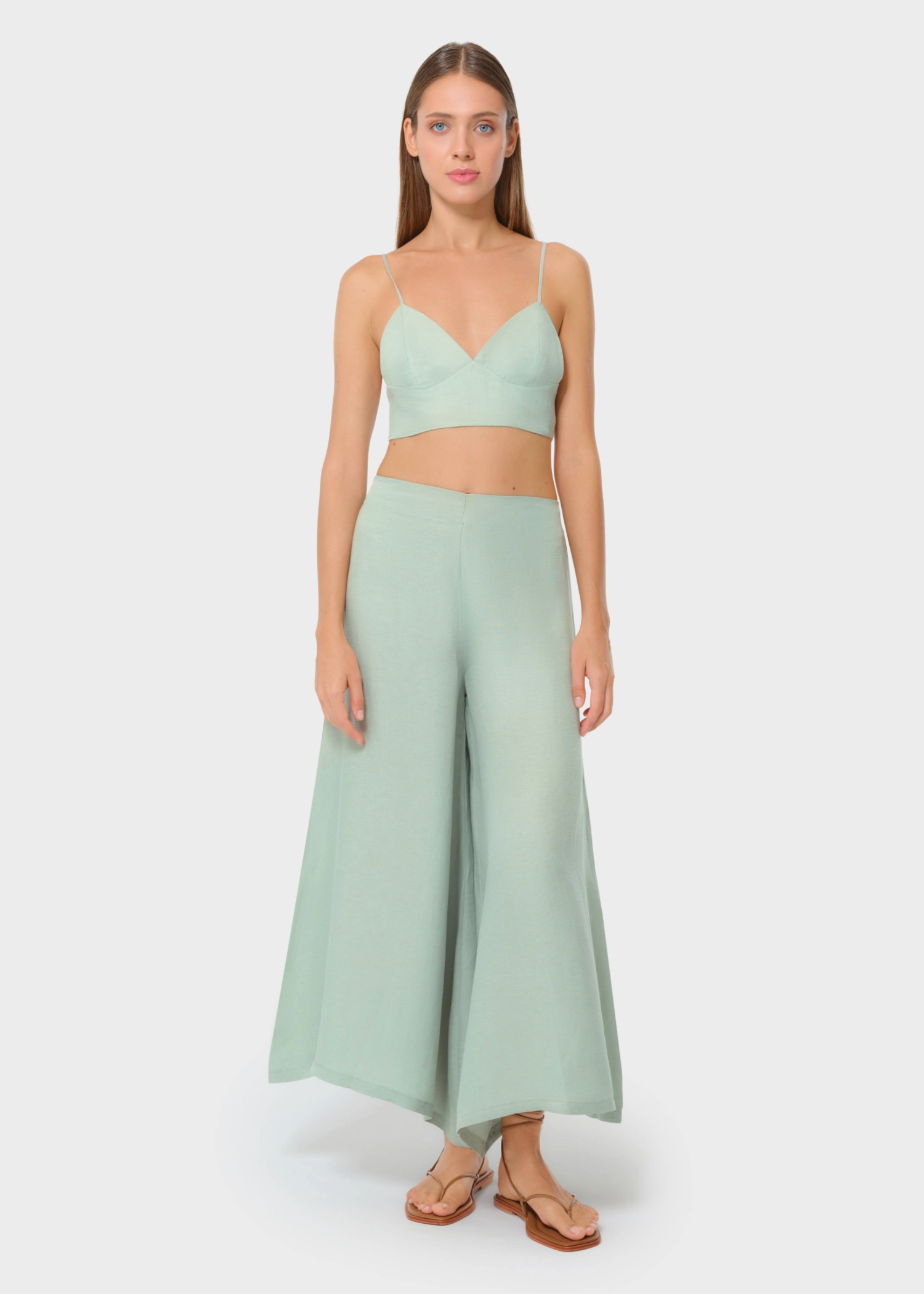 Model wearing a sage green bralette with matching high-waisted wide-leg pants, styled with flat sandals, studio background.