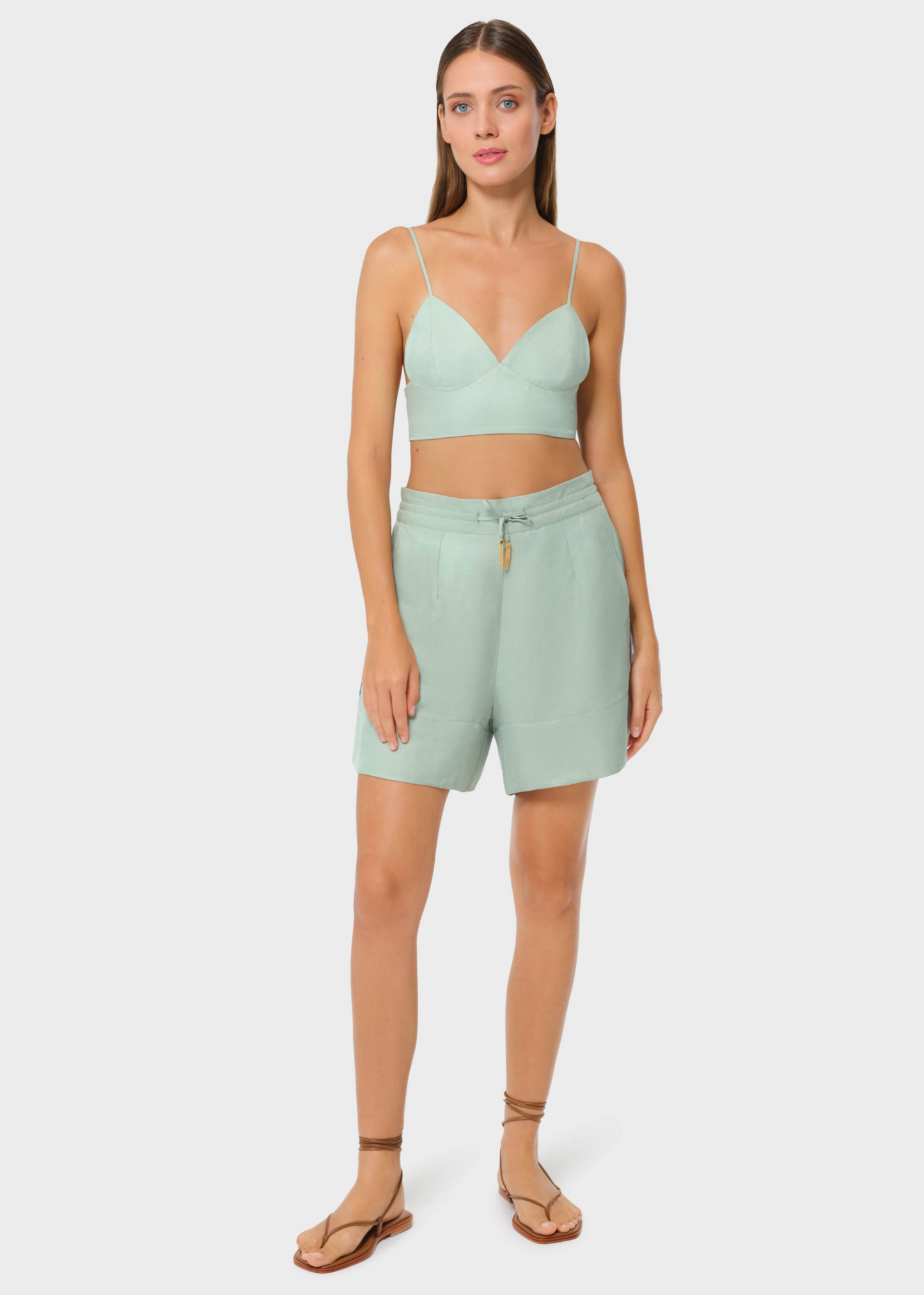 Model wearing sage green bralette with matching lounge shorts on studio background